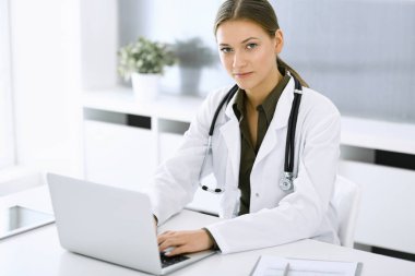 Hastane ofisindeki masada otururken dizüstü bilgisayarda yazan bir kadın doktor. Hekim iş başında. Tıp ve sağlık alanlarındaki veriler