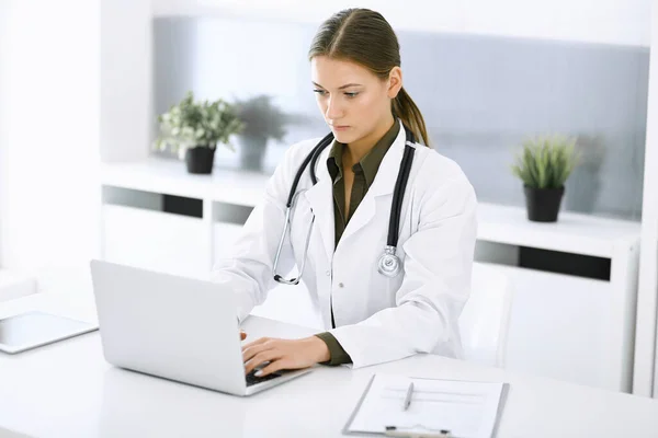 병원 사무실 책상에 앉아 있는 동안 컴퓨터로 타이핑하는 여자 - 의사. 의사 가 직장에 있다. 의학 과 건강 관리에 관한 자료 — 스톡 사진