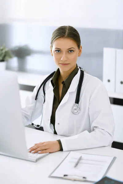 Woman-doctor typing on pc computer while sitting at the desk in hospital office. Physician at work. Data in medicine and healthcare