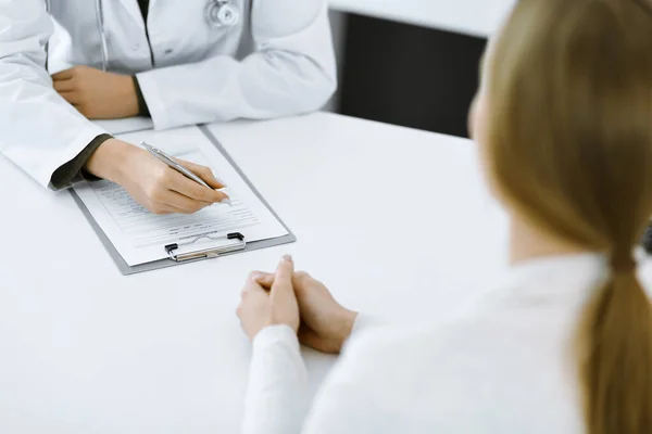 Unbekannte Ärztin und Patientin sitzen und sprechen bei der ärztlichen Untersuchung in der Klinik, aus nächster Nähe. Therapeutin in grüner Bluse füllt Medikamentengeschichte auf. Medizinkonzept — Stockfoto