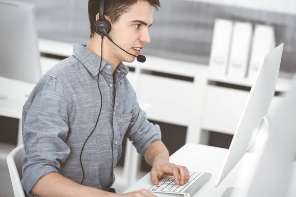 Casual dressed young man using headset and computer while talking with customers online. Call center, business concept — Stock Photo, Image