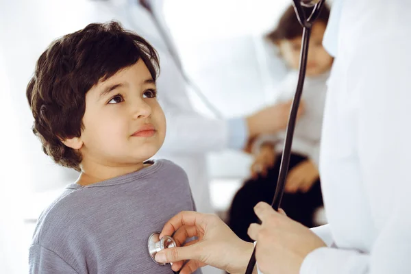 Médico-mujer examinando a un niño paciente por estetoscopio. Lindo chico árabe y su hermano en la cita con el médico. Concepto de medicina — Foto de Stock