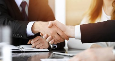 İş adamı, güneşli modern ofiste cam masanın üstünde meslektaşıyla tokalaşıyor. Yakın plan. Toplantıda bilinmeyen iş adamları