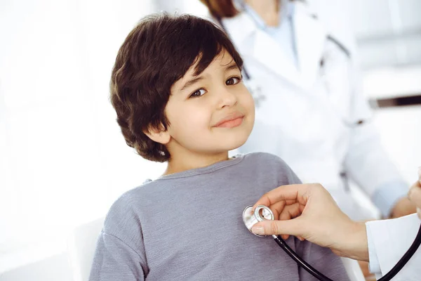 Médico-mujer examinando a un niño paciente por estetoscopio. Lindo chico árabe en la cita con el médico. Concepto de medicina —  Fotos de Stock