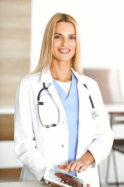 Woman-doctor controls medication history records and exam results while using tablet computer in sunny hospital. Medicine and healthcare concept