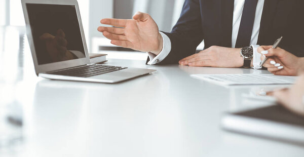 Неизвестные бизнесмены и женщина сидят, работают и обсуждают вопросы на встрече в современном офисе, крупным планом