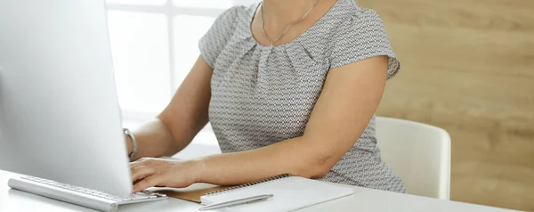 Unknown business woman working with computer while sitting at the desk in modern office, close-up. Middle aged female lawyer or auditor at work
