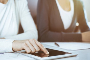 İş kadını, bayan meslektaşına sunum yaparken tablet bilgisayar ekranını işaret ediyor. Ofisteki masada çalışan bir grup iş adamı. Takım çalışması konsepti