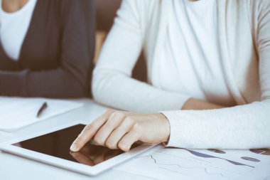 İş kadını, bayan meslektaşına sunum yaparken tablet bilgisayar ekranını işaret ediyor. Ofisteki masada çalışan bir grup iş adamı. Takım çalışması konsepti