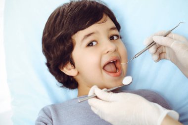 Tatlı Arap çocuk doktorla sözlü kontrol sırasında ağzı açık bir şekilde dişçi koltuğunda oturuyor. Dişçi muayenehanesi. Stomatoloji kavramı