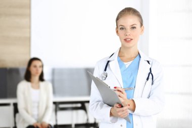 Kadın - doktor hastanın arka planında klinikte tıbbi geçmiş kayıtlarını doldurmak için pano kullanıyor. Tıp konsepti