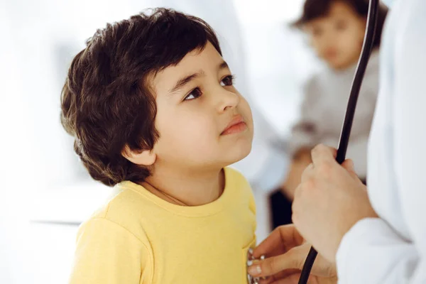 Mujer-médico examinando a un niño paciente por estetoscopio. Lindo chico árabe en la cita con el médico. Medicina ayuda concepto —  Fotos de Stock