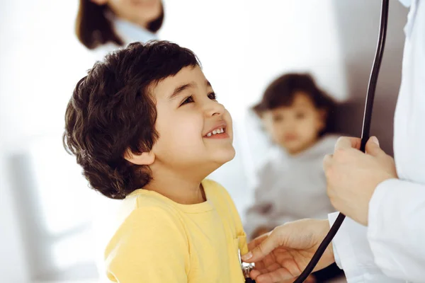 Medico-donna che esamina una paziente infantile mediante stetoscopio. Carino il ragazzo arabo all'appuntamento dal medico. Medicina concetto di aiuto — Foto Stock