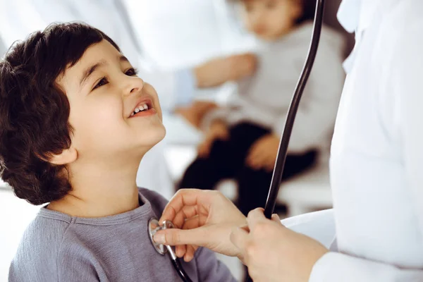 Dokter-vrouw die een kindpatiënt onderzoekt met stethoscoop. Leuke Arabische jongen en zijn broer op afspraak bij de dokter. Geneesmiddelenconcept — Stockfoto