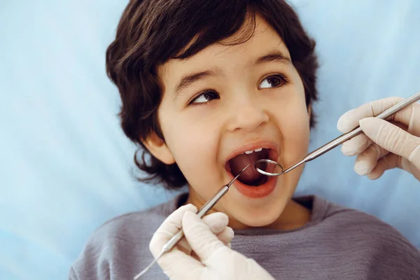 Lindo chico árabe sentado en la silla dental con la boca abierta durante el control oral con el médico. Visita al consultorio del dentista. Concepto de estomatología — Foto de Stock