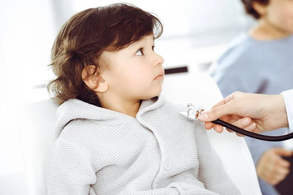 Médico-mujer examinando a un niño paciente por estetoscopio. Lindo chico árabe y su hermano en la cita con el médico. Concepto de medicina —  Fotos de Stock