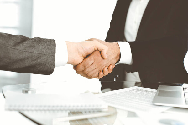 Unknown diverse business people are shaking hands finishing up meeting at the desk in office, close-up. Handshake concept