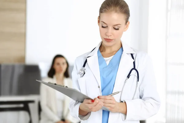 Kvinna - läkare använder Urklipp för att fylla upp medicinering historia rekord form på kliniken i bakgrunden av patienten. Medicinskt koncept — Stockfoto