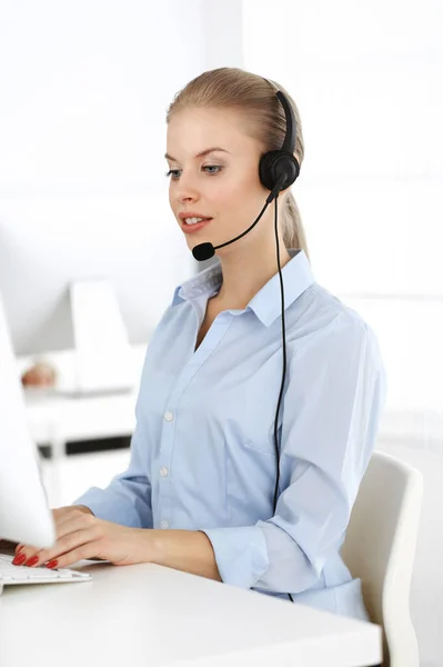 Blond woman call operator is using computer and headset for consulting clients online. Group of diverse people working as customer service occupation. Business concept