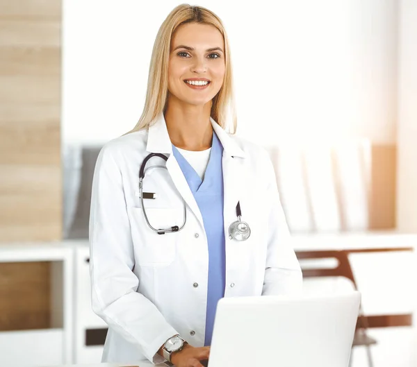 Woman-doctor controls medication history records and exam results while using laptop computer in sunny hospital. Medicine and healthcare concept