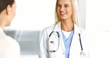 Sunny Hastanesi 'ndeki kadın doktor kadın hastaya danışmaktan mutluluk duyar. Sarışın doktor, pano kullanırken tıbbi geçmişi ve sınav sonuçlarını kontrol ediyor.