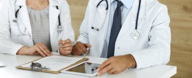 İki bilinmeyen doktor hastane ofisinde masa başında otururken tedavi sorunlarını tartışıyor, yakın plan. Tıptaki veriler