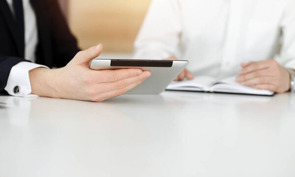 Unknown business people using tablet computer in sunny office. Businessman is working with his colleague at the desk, close-up