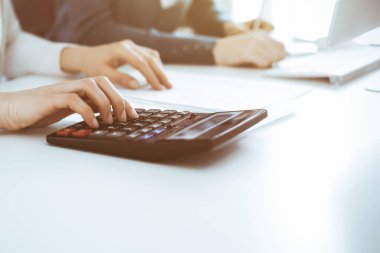 Muhasebeci mali durumu kontrol ediyor ya da vergi formları için hesap makinesi geliri ile sayıyor, eller yakın çekim. İş kadını ofisteki masada iş arkadaşıyla oturuyor ve çalışıyor. Denetim kavramı