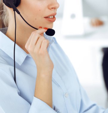 Kadın çağrı operatörü çevrimiçi ve yakın çekim müşterilerine danışmak için bilgisayar ve kulaklık kullanıyor. Müşteri hizmetleri işgali olarak çalışan çeşitli kişiler grubu