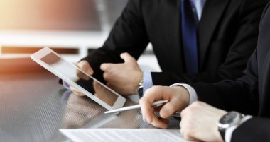 Businessman using tablet computer and work together with his colleague in sunny modern office, close-up. Unknown business people at meeting. Teamwork and partnership concept