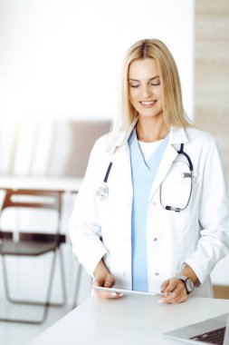 Kadın doktor, güneşli hastanede tablet bilgisayar kullanırken ilaç geçmişi ve sınav sonuçlarını kontrol ediyor. Tıp ve sağlık hizmetleri kavramı