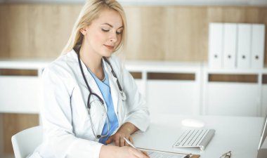 Hastanedeki ya da klinikteki masa başında oturan kadın doktor. Sarışın, neşeli doktor ilaç geçmişi formunu dolduruyor.