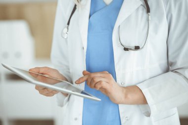 Bilinmeyen kadın doktor klinikte duruyor ve tablet bilgisayar kullanıyor, yakın plan. Veriler ve tıp ve sağlık hizmetlerindeki en iyi hizmet