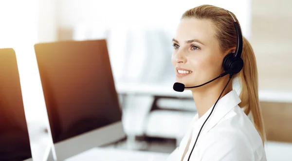 Blond kvinnlig kundtjänst representant konsulterar kunder online med headset i soligt kontor. Begreppet callcenter — Stockfoto