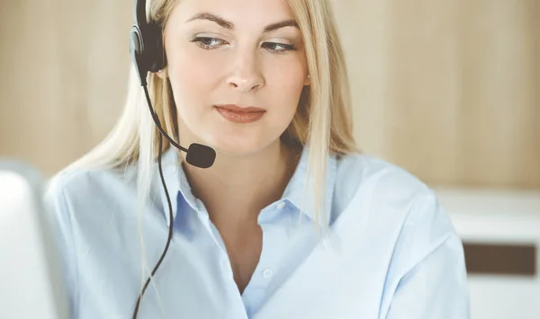 Blonde business woman sitting and communicated by headset in call center office. Concept of telesales business or home office occupation Stock Image