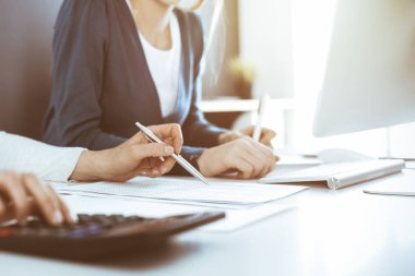 Muhasebeci mali durumu kontrol ediyor ya da vergi formları için hesap makinesi geliri ile sayıyor, eller yakın çekim. İş kadını ofisteki masada iş arkadaşıyla oturuyor ve çalışıyor. Denetim kavramı