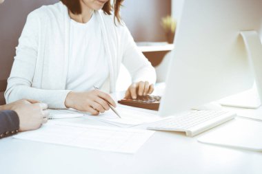 Muhasebeci mali durumu kontrol ediyor ya da vergi formları için hesap makinesi geliri ile sayıyor, eller yakın çekim. İş kadını ofisteki masada iş arkadaşıyla oturuyor ve çalışıyor. Denetim kavramı