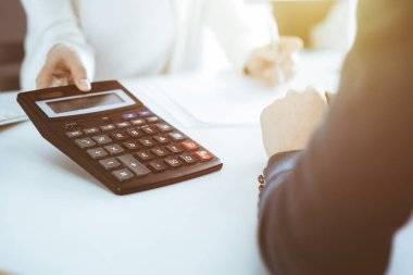 Muhasebeci mali durumu kontrol ediyor ya da vergi formları için hesap makinesi geliri ile sayıyor, eller yakın çekim. İş kadını ofisteki masada iş arkadaşıyla oturuyor ve çalışıyor. Denetim kavramı