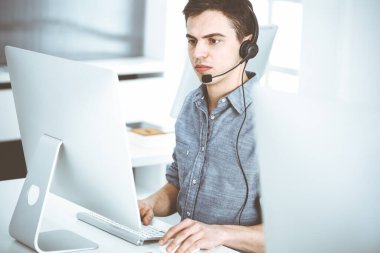 İnternette müşterilerle konuşurken kulaklık ve bilgisayar kullanan sıradan giyinmiş genç bir adam. Çağrı merkezi, iş konsepti