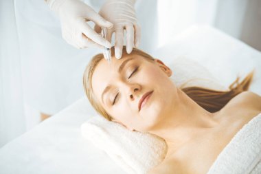 Güzellik doktoru sarışın kadın yüzüne şırıngayla güzellik prosedürü uyguluyor. Kozmetik tıp, güzellik enjeksiyonu konsepti