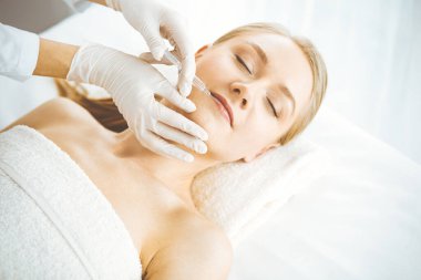 Güzellik doktoru sarışın kadın yüzüne şırıngayla güzellik prosedürü uyguluyor. Kozmetik tıp, güzellik enjeksiyonu konsepti