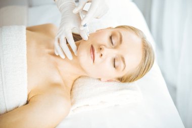 Güzellik doktoru sarışın kadın yüzüne şırıngayla güzellik prosedürü uyguluyor. Kozmetik tıp, güzellik enjeksiyonu konsepti