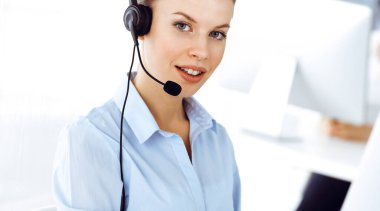 Sarışın kadın çağrı operatörü müşterilere danışmak için bilgisayar ve kulaklık kullanıyor. Müşteri hizmetleri işgali olarak çalışan bir grup insan. İş konsepti