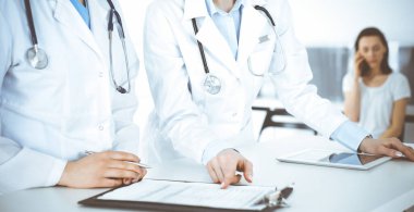 İş yerindeki bilinmeyen kadın doktorlar, arka planda hastaları var. Hastane resepsiyonunda beklerken tıbbi belgeleri dolduran kadın doktorlar, yakın plan. Sağlık hizmeti kavramı