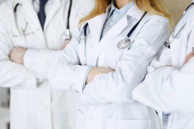 Hastane ofisinde kolları kavuşturulmuş bir ekip olarak bekleyen bir grup doktor, yakın plan. Tıbbi yardım, sağlık sigortası ve tıp konsepti