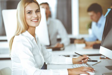 Modern ofisteki işyerinde bilgisayar kullanan bir iş kadını. Sekreter ya da kadın avukat gülümsüyor ve mutlu görünüyor. Zevk ve başarı için çalışmak