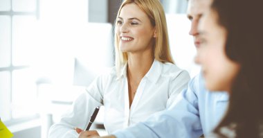 Bir grup iş adamı toplantıda soruları tartışıyor. Ofis görüşmelerinde iş arkadaşına gülümseyen sarışın iş kadınının vesikalığı. Şirket işgalinde takım çalışması ve işbirliği