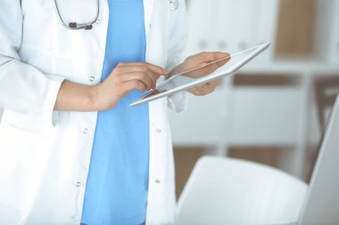 Bilinmeyen kadın doktor klinikte duruyor ve tablet bilgisayar kullanıyor, yakın plan. Veriler ve tıp ve sağlık hizmetlerindeki en iyi hizmet