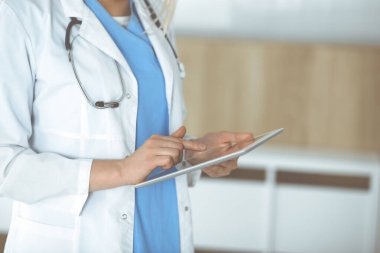Bilinmeyen kadın doktor klinikte duruyor ve tablet bilgisayar kullanıyor, yakın plan. Veriler ve tıp ve sağlık hizmetlerindeki en iyi hizmet