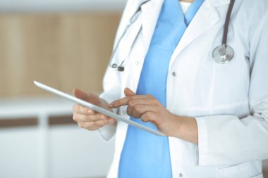 Bilinmeyen kadın doktor klinikte duruyor ve tablet bilgisayar kullanıyor, yakın plan. Tıp ve sağlık alanlarındaki veriler